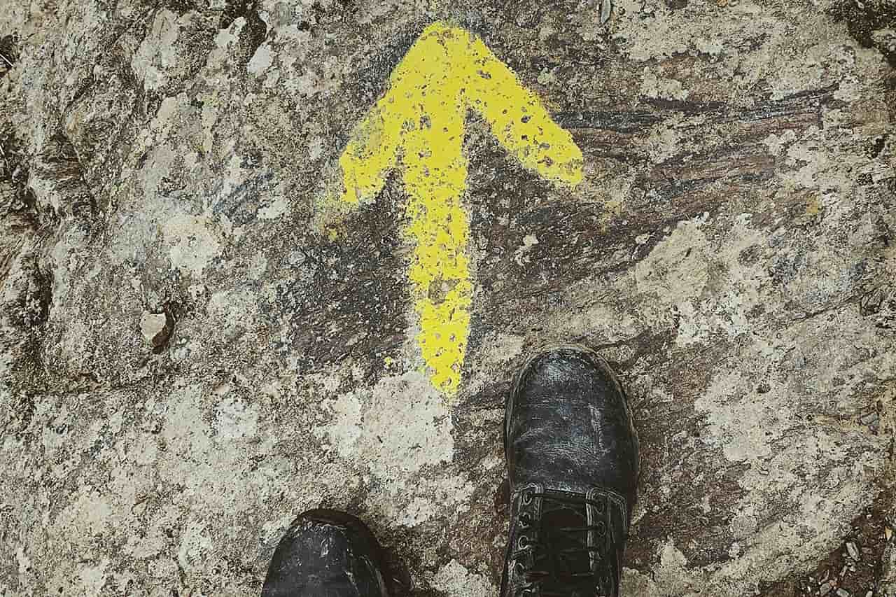 Los pies de un peregrino se paran ante una flecha amarilla que señala hacia Santiago de Compostela